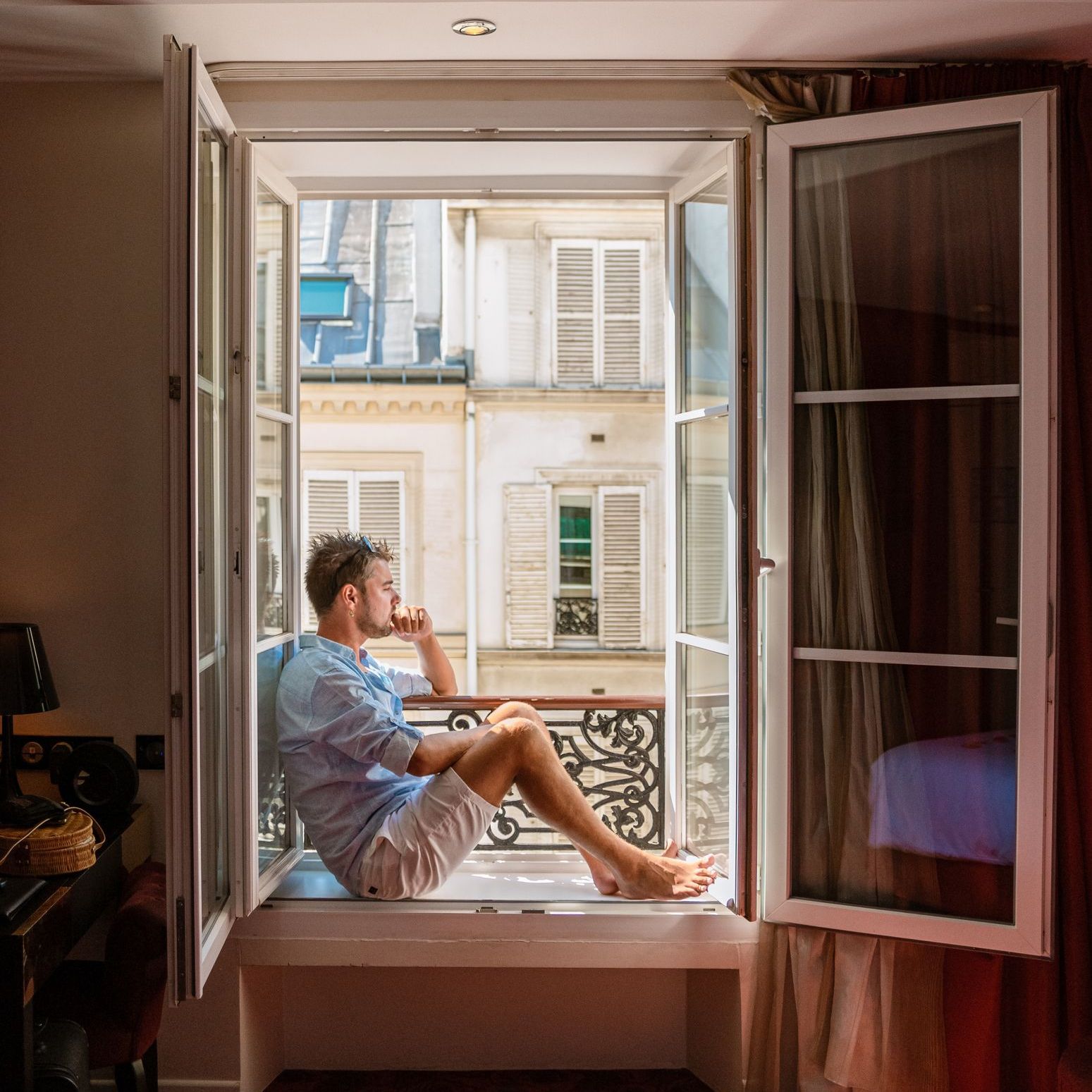 young man sitting in a window looking out over the city of Paris. Men enjoy the sun in the window of a hotel room. Men in the morning by the window in the bedroom